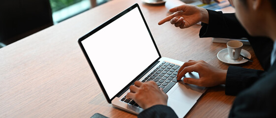 A businessman is using a computer laptop with a white blank screen at the meeting table.