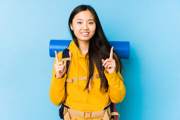 Young chinese backpacker woman isolated indicates with both fore fingers up showing a blank space.
