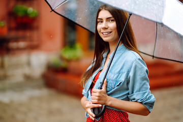 Cheerful woman  under a transparent umbrella enjoying rainfall. Young woman hiding from the rain....