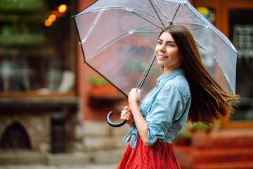 Cheerful woman  under a transparent umbrella enjoying rainfall. Young woman hiding from the rain....