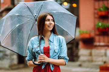 Cheerful woman  under a transparent umbrella enjoying rainfall. Young woman hiding from the rain....