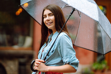 Cheerful woman  under a transparent umbrella enjoying rainfall. Young woman hiding from the rain....