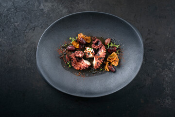 Modern style traditional Italian polpo alla griglia with barbecued octopus, olives and vegetable chips offered as top view on a modern design plate with copy space