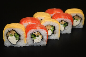 Multicolored sushi roll with salmon, cheese, cucumber and omelet on black background.