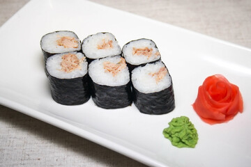 Sushi maki with tuna on a white dish with wasabi and ginger.