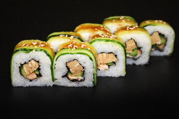 Sushi roll with cucumber, omelette and unagi sauce on a black background.