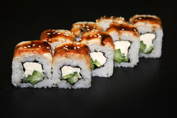 Sushi roll with eel and unagi sauce on a black background.