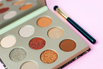 Multi-colored pastel brown red eye shadow on a pink background with brushes.