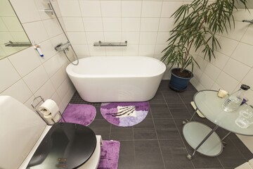 Interior view of modern private bathroom. White tiled walls and black tiled floor and white plumbing. 