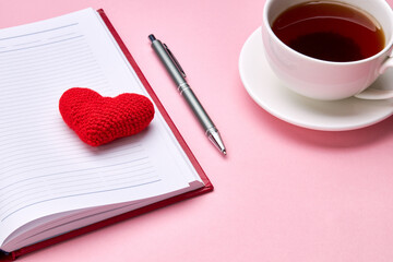 above view for pink desk with diary, tea cup and heart symbol. romance background backdrop