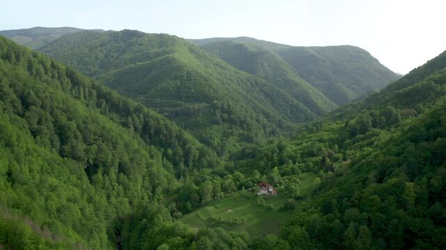 Drone flight above green tree-covered mountain slopes and houses nestled in them, the Balkan Mountains, Bulgaria