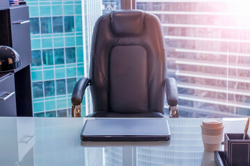 View of empty workplace in office. The chair sits next to the glass table on which the laptop is....