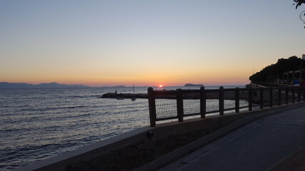 Sunset view from the Mediterranean coast. Sunset visible over the breakwater in the calm sea on the horizon. Mediterranean waves calmly hitting the shore. Mediterranean sea with beautiful sunset.