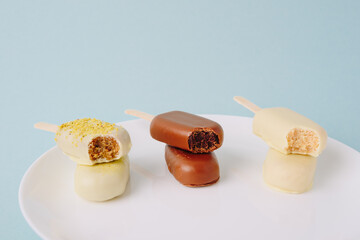 Chocolate cake in the form of ice cream on a stick on a white plate and a colored background