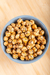 Roasted, yellow chickpeas in ceramic bowl on wooden background.