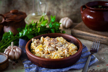 Lunch is hearty: stewed potatoes with mushrooms in a clay plate on a gray background