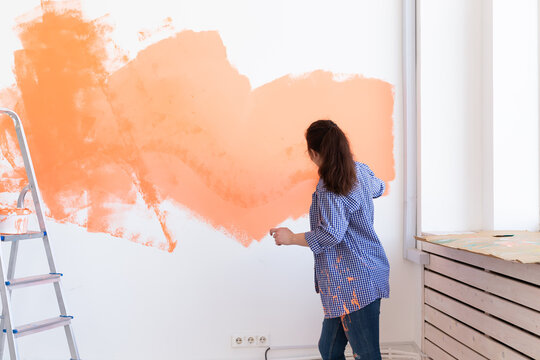 Happy smiling woman painting interior wall of new house. Redecoration, renovation, apartment repair and refreshment concept.