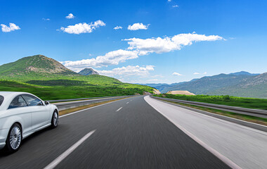 Fototapeta premium A white car rushes along the road against the backdrop of a beautiful countryside landscape.