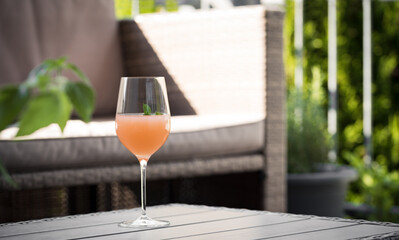 Orange Aperitif with mint standing on an outdoor table, a garden lounge and plants in the background standing for an enjoyable evening