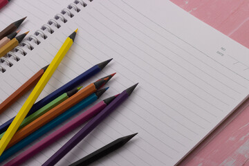 Multicolor blackwood pencils are laid out on a spiral notebook on a pink background. Back to school. Copy space