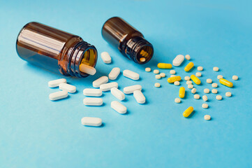 Two opened bottles with tablets and capsules on blue background, selective focus.
