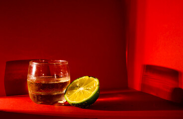 Vaso de ron con unas rodajas de limón. La imagen tiene un fondo rojo y en el cual se reflejan...