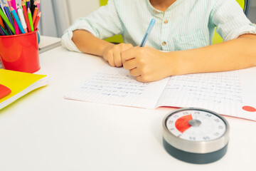 Little boy with lesson timer while doing writing exercise on background