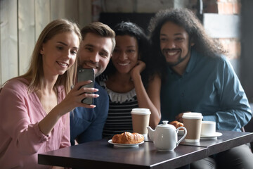 Happy diverse people taking selfie for social network, sitting at table in cafe, smiling young woman holding smartphone, photographing, posing for photo with friends, vlogger recording video