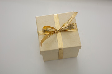 Beige closed gift box with gold color ribbon isolated on gray background. Closeup, high angle view.