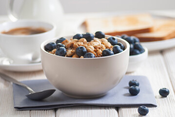 Breakfast with granola and blueberry, milk with orange juice and baked toasts on the white wooden table close-up