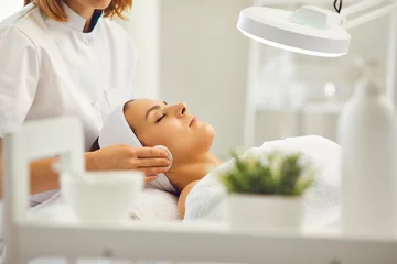 Store enrouleur Salon de beauté Cosmetologist cleaning womans face with cotton pads in beauty salon