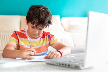 Little boy doing homework in front of a laptop. Concept of online education from home.