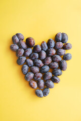 Heart made of ripe plums. Plums on yellow background. Healthy food.