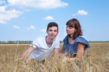 Naklejka na ściany i meble Single mother looking with love at her teen age son, people sitting on wheat field