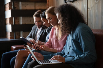 Diverse people using gadgets together, sitting on couch in row, friends chatting, surfing internet, sharing news, looking at electronic devices screen, watching video in social network