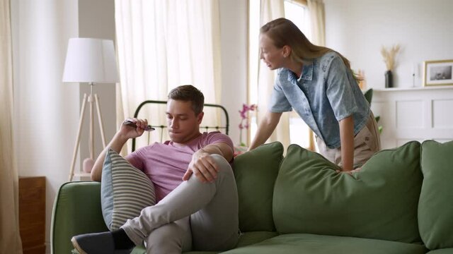 young woman starts yelling on husband laying on couch. wife quarrels angrily with man due to offend and disappointment. upset girlfriend shouts at boyfriend emotionally, man is nervous, listening