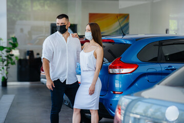 Young couple in masks selects a new vehicle and consult with a representative of the dealership in the period of the pandemic. Car sales, and life during the pandemic