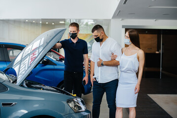 Young couple in masks selects a new vehicle and consult with a representative of the dealership in the period of the pandemic. Car sales, and life during the pandemic