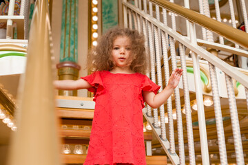 Funny little curly girl in a red dress on the stairs with flashlights