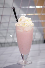 Strawberry milkshake with whipped cream and a tube on the bar.