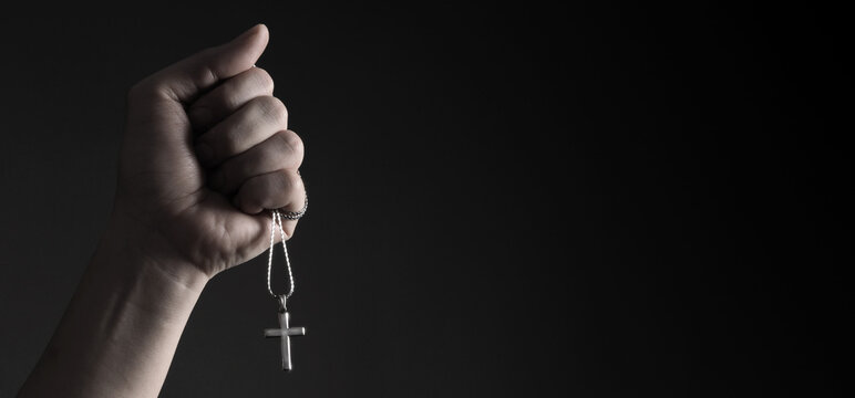 Crucifix pendant or cross sign made from silver and hold in man hand. represent praying for someone that pass away from World pandemic coronavirus and close-up shot black background 