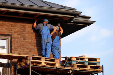 Workers during roofing, two builders on scaffolding standing near the building wall. Construction and repair works of a house