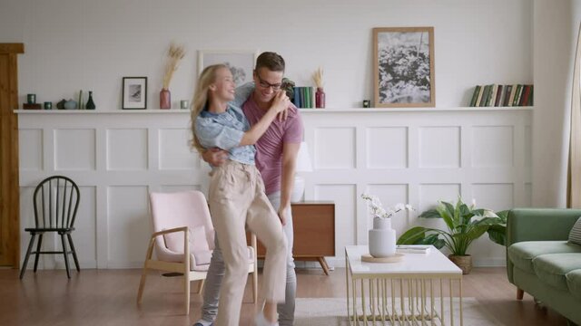 young man carry in his lovely wife to new apartment, blonde woman is excited and happy. husband shows rented house for holiday, wife is surprised, married couple hug