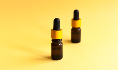Two bottles of yellow cosmetic oil against yellow background