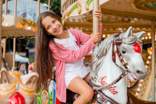 A teenage girl with long hair rolls around on a swing horse carousel. Sitting on a horse at an amusement park