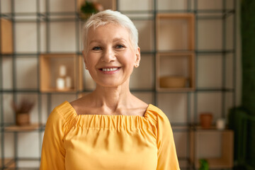 Portrait of joyful stylish middle aged woman with short haircut posing indoors expressing positive...