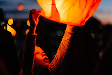 The child starts the lanterns into the sky on a dark night. Celebration, traditions of the new year.