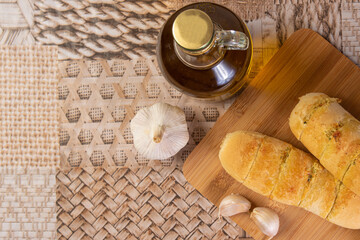 Fototapeta na wymiar Garlic bread stuffed with cheese arranged on a cutting board with garlic around it and a bottle of olive oil on a table, Top view.