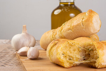 Garlic bread stuffed with cheese arranged on a cutting board with garlic around it and a bottle of...