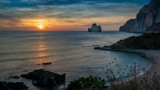 Timelapse at sunset in the suggestive setting of the Masua stream, overlooking the imposing rock of the Pan di Zucchero, along the Iglesiente coast in the southwest of Sardinia, Italy.